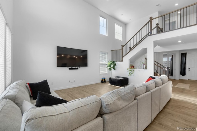 living room featuring baseboards, recessed lighting, stairs, a towering ceiling, and light wood-type flooring