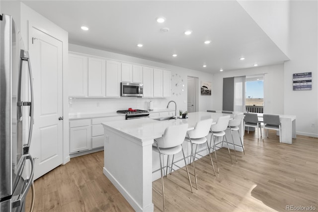 kitchen with an island with sink, a sink, appliances with stainless steel finishes, a breakfast bar area, and decorative backsplash