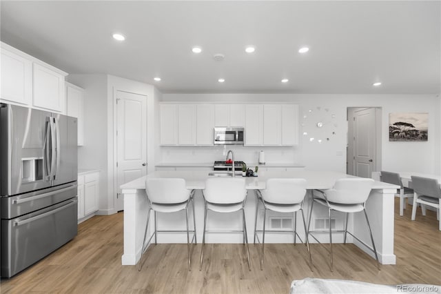 kitchen with an island with sink, stainless steel appliances, light countertops, light wood-style floors, and white cabinetry