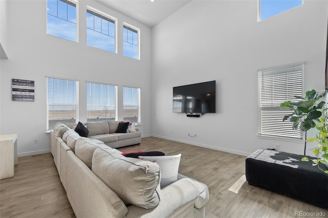 living area with baseboards, a high ceiling, and light wood-style floors