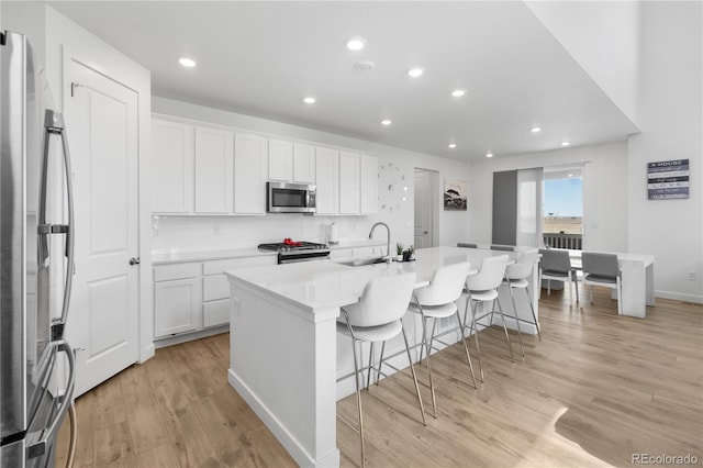 kitchen with an island with sink, a kitchen breakfast bar, stainless steel appliances, a sink, and light wood-style flooring