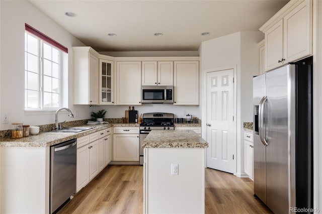 kitchen with a center island, appliances with stainless steel finishes, sink, white cabinets, and light hardwood / wood-style flooring