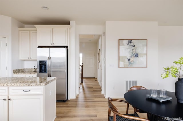 kitchen featuring light hardwood / wood-style flooring, stainless steel refrigerator with ice dispenser, light stone counters, and white cabinets