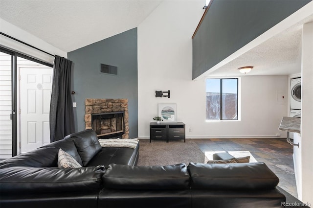 living room with vaulted ceiling, stacked washing maching and dryer, a textured ceiling, and a fireplace