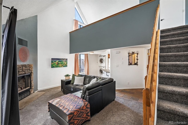 carpeted living room with visible vents, high vaulted ceiling, a fireplace, stacked washer / drying machine, and stairs