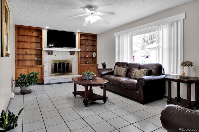 living room featuring built in shelves, light tile patterned flooring, a textured ceiling, and a tiled fireplace