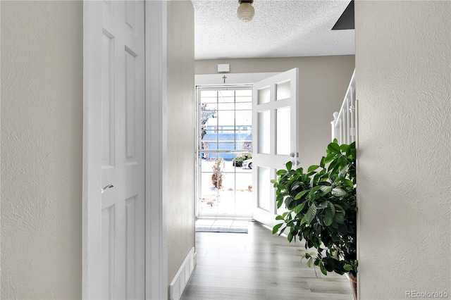 interior space featuring visible vents, a textured wall, a textured ceiling, and wood finished floors