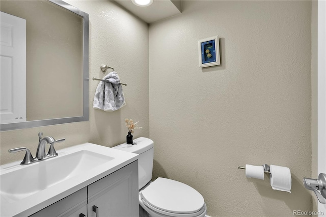 bathroom featuring a textured wall, vanity, and toilet