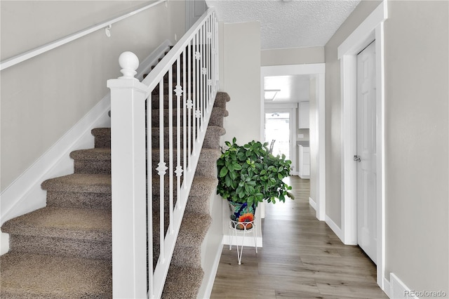 stairway with a textured ceiling, baseboards, and wood finished floors