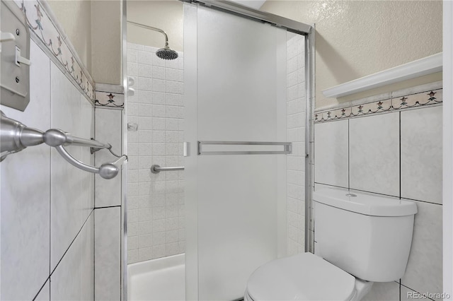 bathroom with a shower stall, toilet, and tile walls