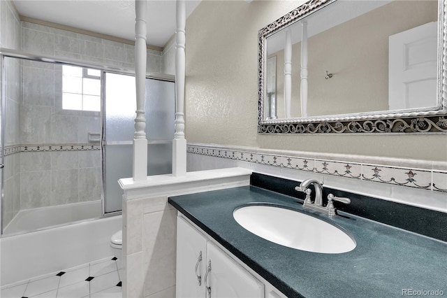 full bathroom with enclosed tub / shower combo, a textured wall, toilet, and vanity