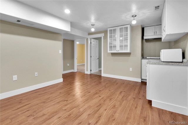 kitchen with baseboards, light wood-style flooring, visible vents, and white cabinetry