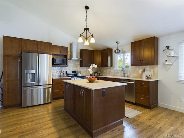 kitchen featuring wall chimney exhaust hood, a kitchen island, appliances with stainless steel finishes, light countertops, and pendant lighting