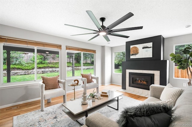 8288 W Chestnut Ave, Littleton, CO 80128 - living area featuring plenty of natural light, light wood-type flooring, a tiled fireplace, a textured ceiling, and ceiling fan