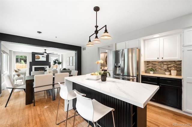 8288 W Chestnut Ave, Littleton, CO 80128 - kitchen featuring stainless steel refrigerator with ice dispenser, white cabinetry, backsplash, a kitchen island, and pendant lighting