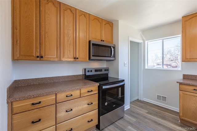 kitchen featuring dark countertops, visible vents, baseboards, light wood-type flooring, and appliances with stainless steel finishes