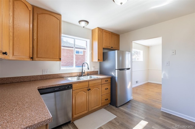 kitchen with a sink, light wood-type flooring, baseboards, and appliances with stainless steel finishes