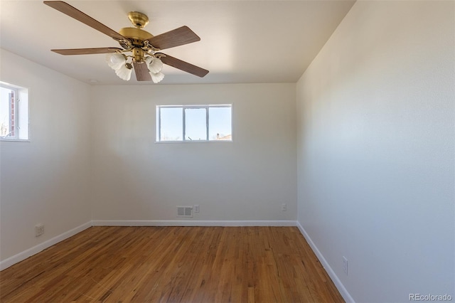 empty room with wood finished floors, baseboards, visible vents, and a wealth of natural light