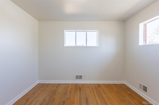 unfurnished room with wood finished floors, visible vents, and baseboards