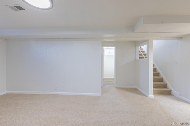 finished basement featuring light carpet, visible vents, stairway, and baseboards