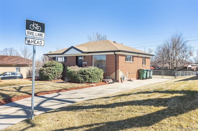 view of front facade with brick siding, a shingled roof, a front yard, and fence