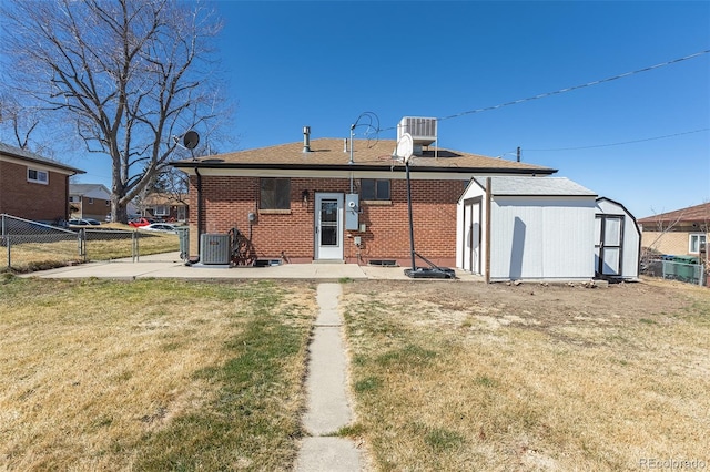 rear view of house with a storage unit, fence, a yard, brick siding, and central AC unit