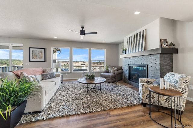 living area with ceiling fan, a glass covered fireplace, a healthy amount of sunlight, and wood finished floors