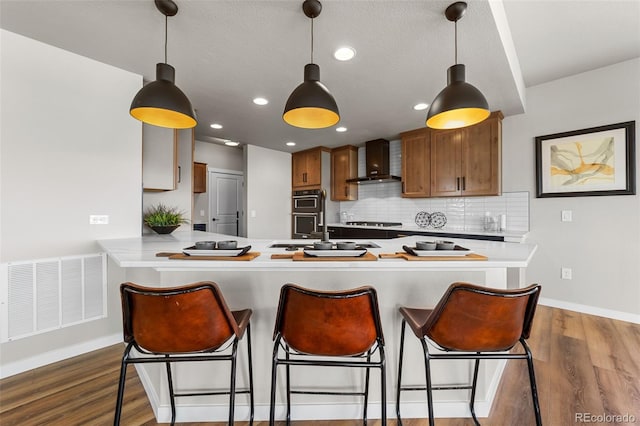 kitchen with visible vents, a sink, dark wood finished floors, double oven, and wall chimney exhaust hood