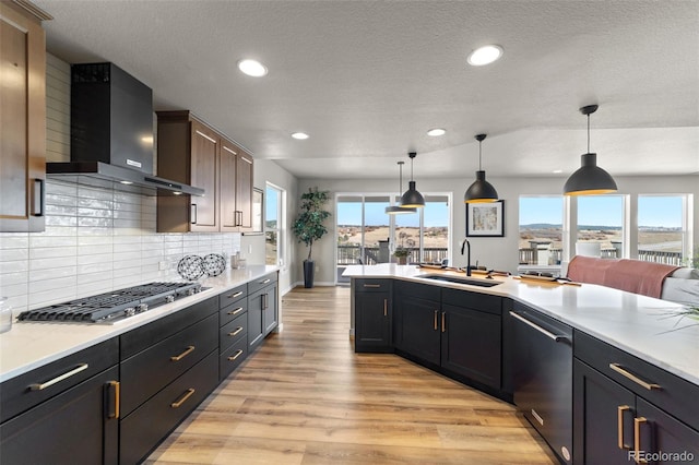 kitchen featuring light wood finished floors, light countertops, appliances with stainless steel finishes, wall chimney exhaust hood, and a sink