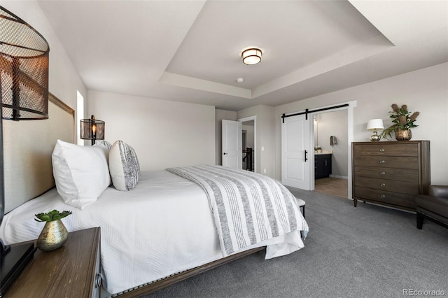 carpeted bedroom with a tray ceiling, a barn door, and connected bathroom