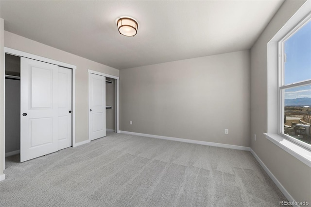 unfurnished bedroom with light colored carpet, multiple closets, and baseboards