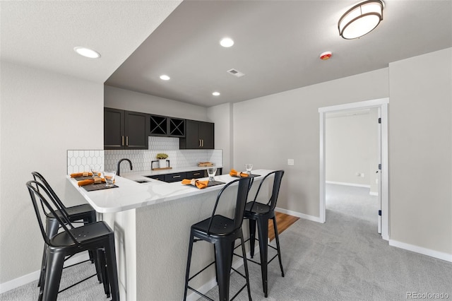 kitchen with a peninsula, a kitchen breakfast bar, backsplash, and a sink