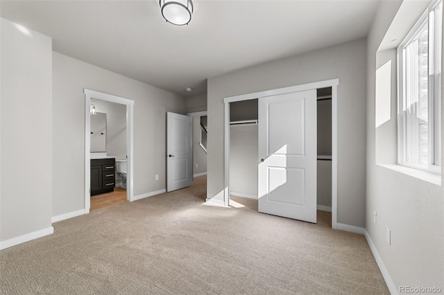 unfurnished bedroom featuring light colored carpet, baseboards, a closet, and ensuite bathroom