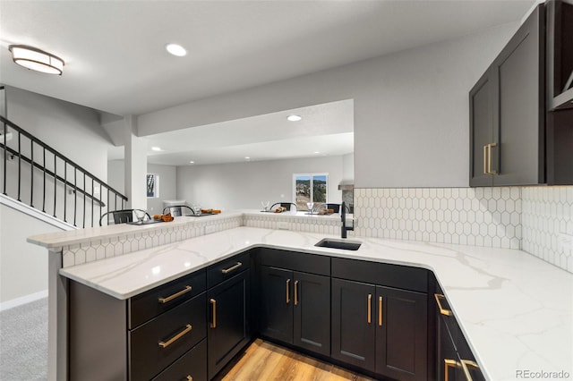 kitchen with decorative backsplash, a peninsula, light stone countertops, and a sink