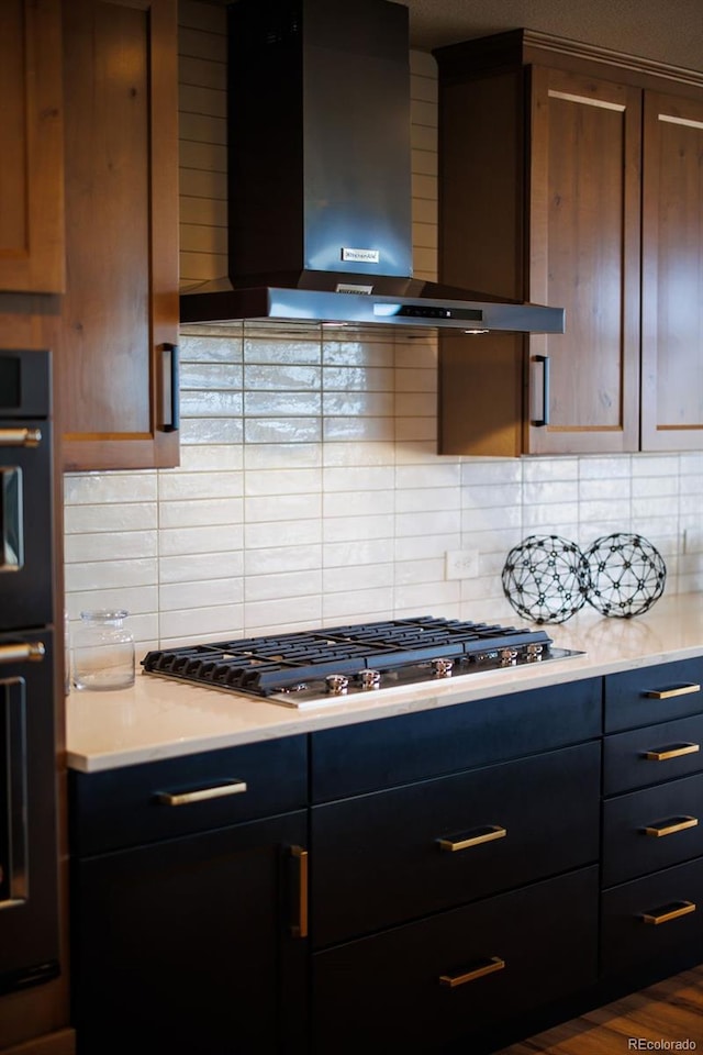 kitchen featuring stainless steel gas cooktop, decorative backsplash, light countertops, and wall chimney exhaust hood