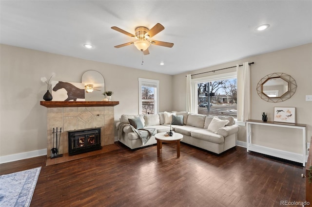 living room featuring dark wood-type flooring, ceiling fan, and a tiled fireplace