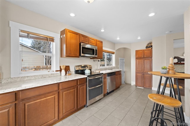 kitchen featuring light tile patterned flooring, a kitchen bar, sink, appliances with stainless steel finishes, and light stone countertops