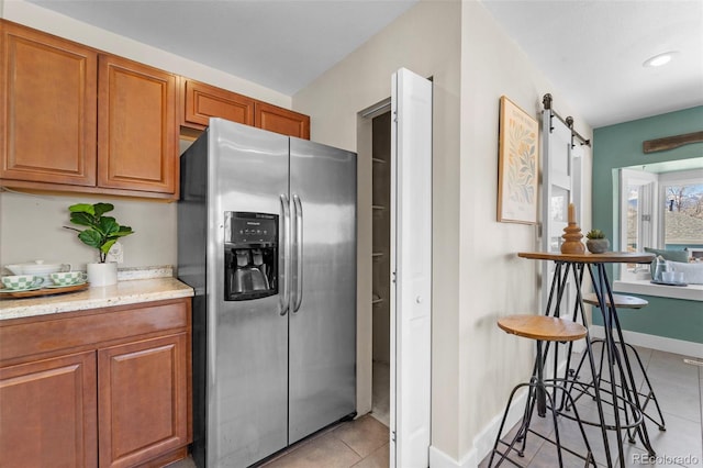 kitchen featuring stainless steel refrigerator with ice dispenser, a barn door, light tile patterned floors, and light stone counters