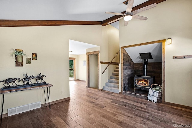 living room featuring beam ceiling, dark wood-type flooring, ceiling fan, and a wood stove