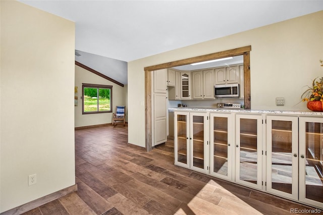 kitchen with lofted ceiling, dark hardwood / wood-style floors, cream cabinets, and stove