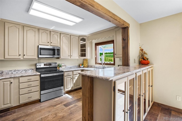 kitchen with sink, dark wood-type flooring, appliances with stainless steel finishes, light stone counters, and kitchen peninsula