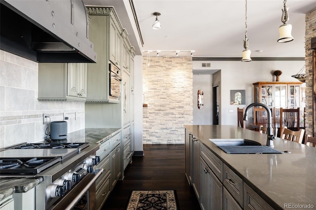 kitchen with a sink, under cabinet range hood, dark wood finished floors, stovetop, and decorative backsplash