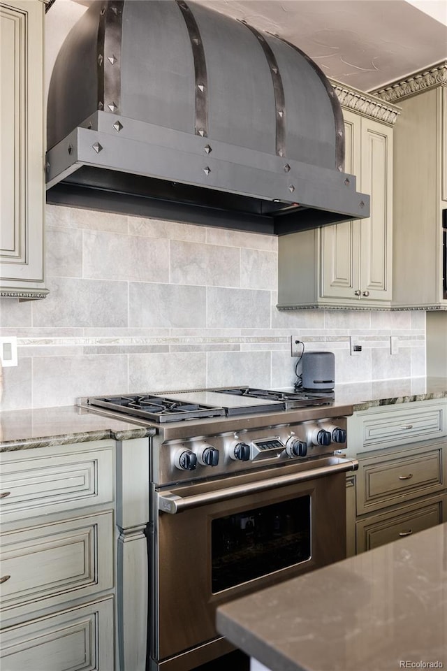 kitchen featuring backsplash, cream cabinets, stainless steel stove, and wall chimney range hood