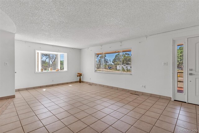 207 Autobee Ln, Avondale, CO 81022 - spare room featuring healthy amount of natural light, a textured ceiling, tile patterned floors, and baseboards