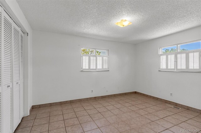 207 Autobee Ln, Avondale, CO 81022 - unfurnished bedroom with multiple windows, a textured ceiling, a closet, light tile patterned floors, and baseboards