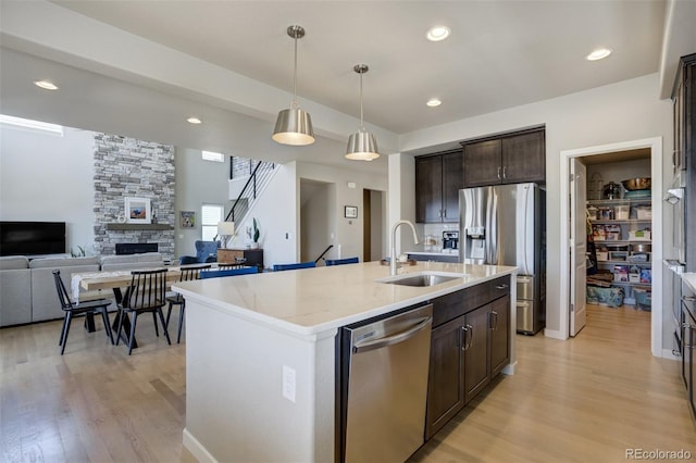 10024 Waterton Canyon Way, Colorado Springs, CO 80924 - kitchen with dark brown cabinetry, light wood-type flooring, a fireplace, stainless steel appliances, and a sink