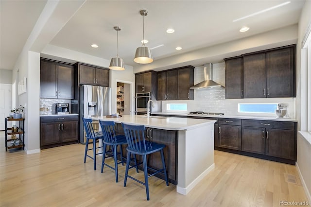 10024 Waterton Canyon Way, Colorado Springs, CO 80924 - kitchen with wall chimney range hood, light wood-style flooring, dark brown cabinets, a breakfast bar area, and appliances with stainless steel finishes