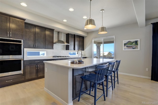 10024 Waterton Canyon Way, Colorado Springs, CO 80924 - kitchen featuring light wood-style floors, wall chimney exhaust hood, a breakfast bar, stainless steel appliances, and baseboards