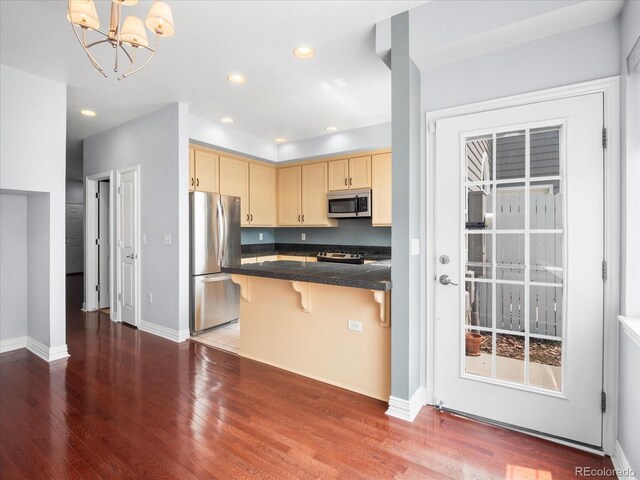 kitchen with light brown cabinetry, hardwood / wood-style floors, a breakfast bar, an inviting chandelier, and stainless steel appliances