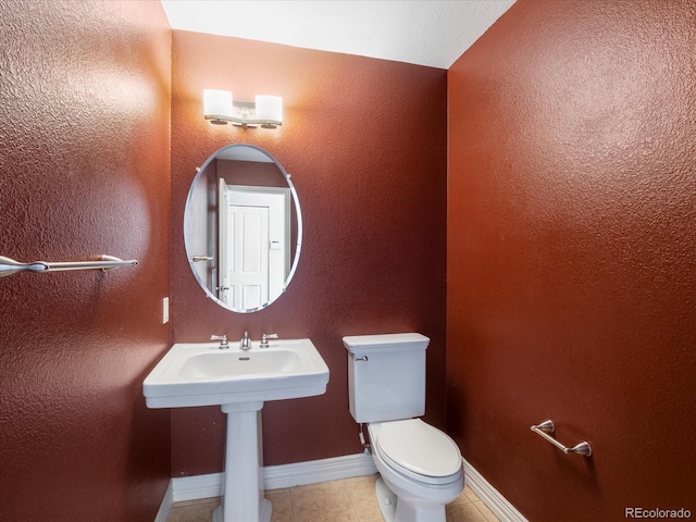 half bathroom with a textured wall, tile patterned flooring, toilet, and baseboards